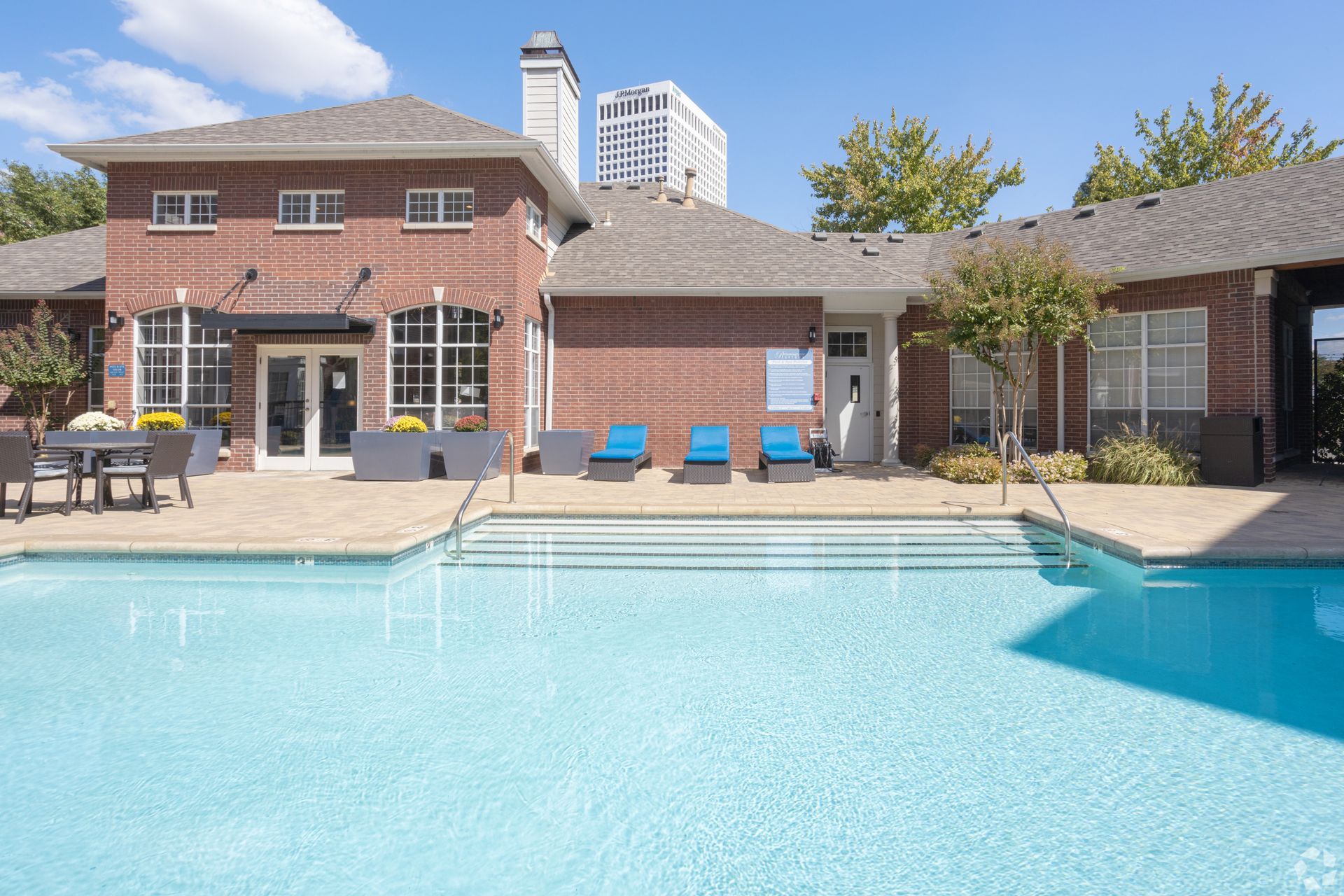 Apartment courtyard with a swimming pool, lounge chairs, and brick buildings under a blue sky