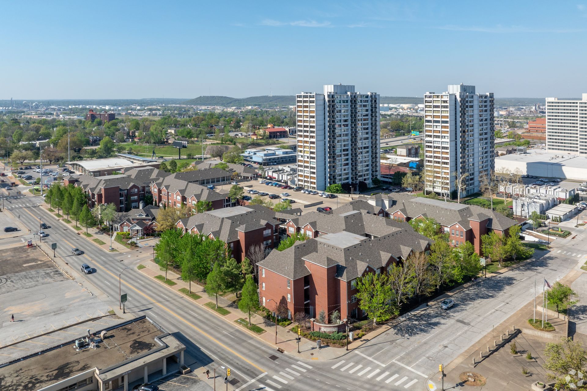 Aerial view of a city block with apartment towers, brick buildings, streets, and a rail line under a clear sky
