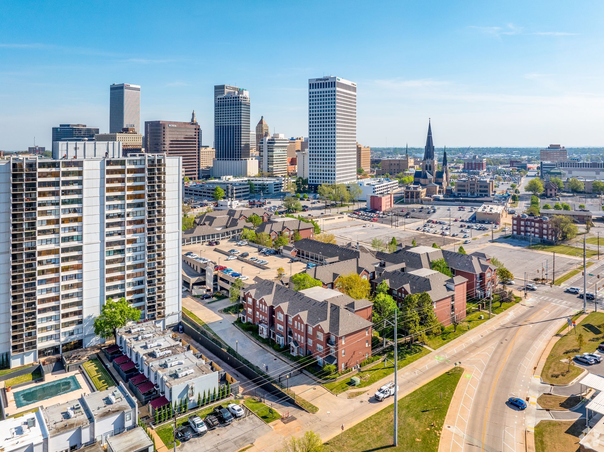 Aerial view of a modern city skyline with high-rise apartments, roads, and a bright blue sky.