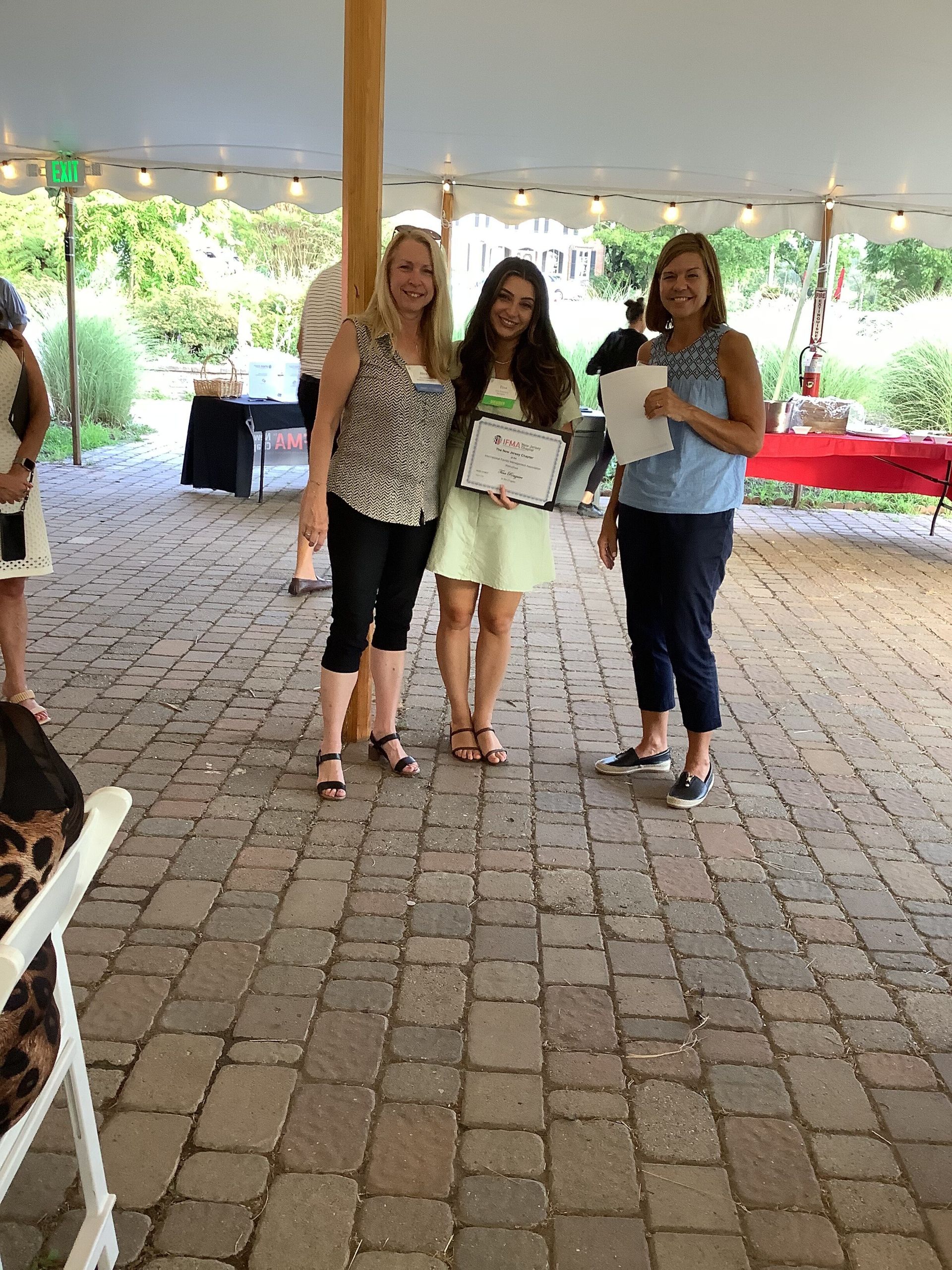 Three women are posing for a picture under a tent.