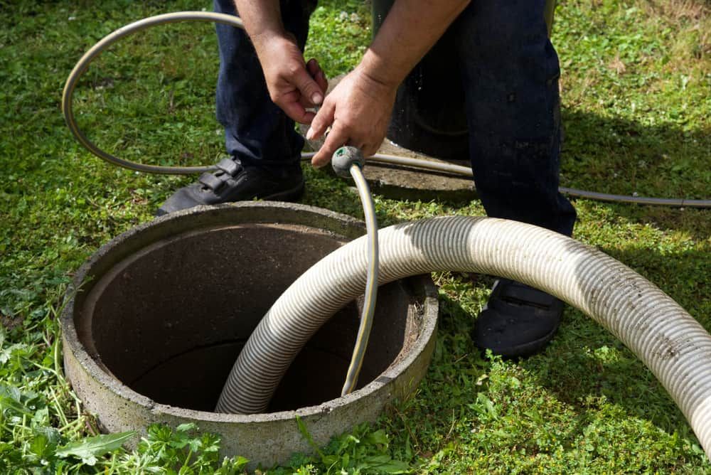 A Man Is Pumping A Hose Into A Septic Tank — Peel Valley Plumbing In Hillvue, NSW