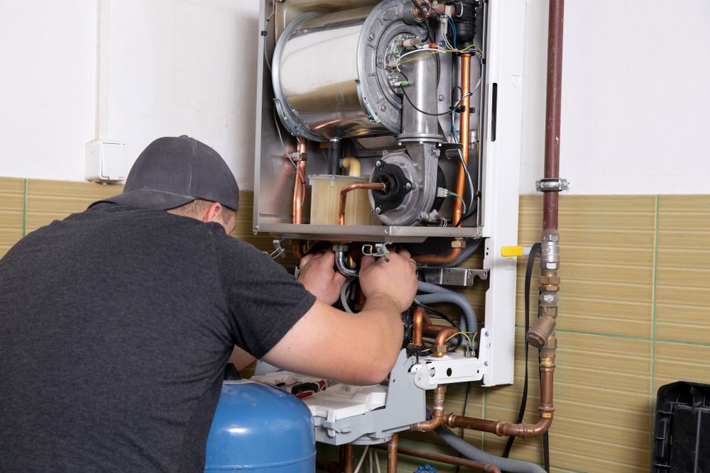 A Man is Working on a Boiler in a Garage — Peel Valley Plumbing In Hillvue, NSW