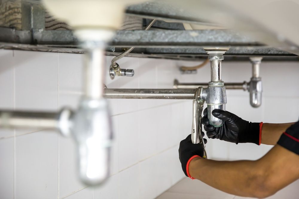 A Plumber is Fixing a Sink Pipe in a Bathroom — Peel Valley Plumbing In Hillvue, NSW