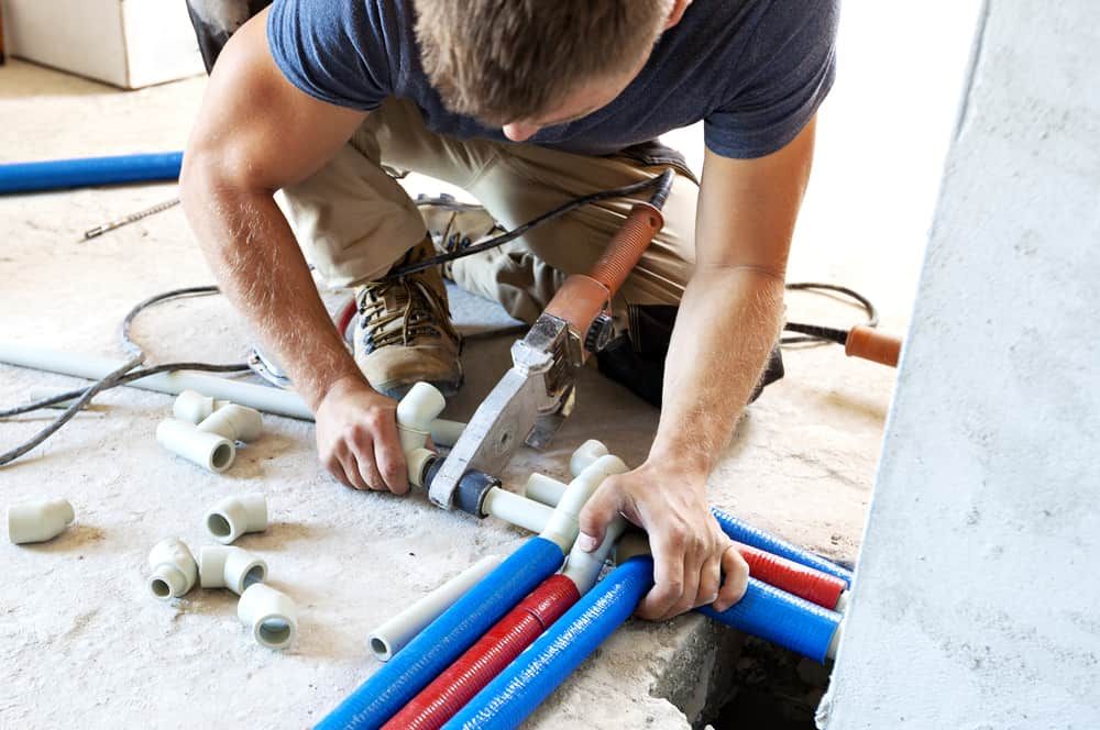 A Man Is Kneeling On The Floor Working On Pipes — Peel Valley Plumbing In Hillvue, NSW