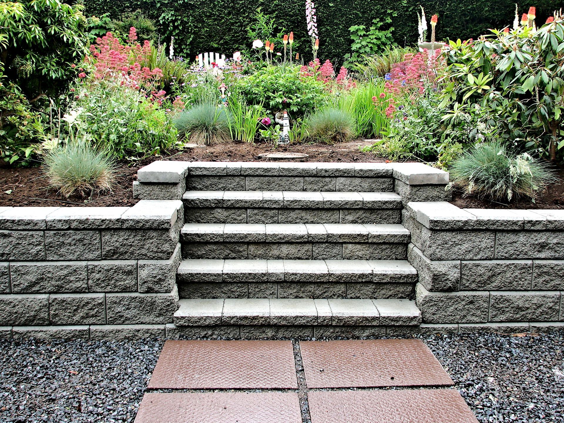 A stone wall with stairs leading up to a garden.