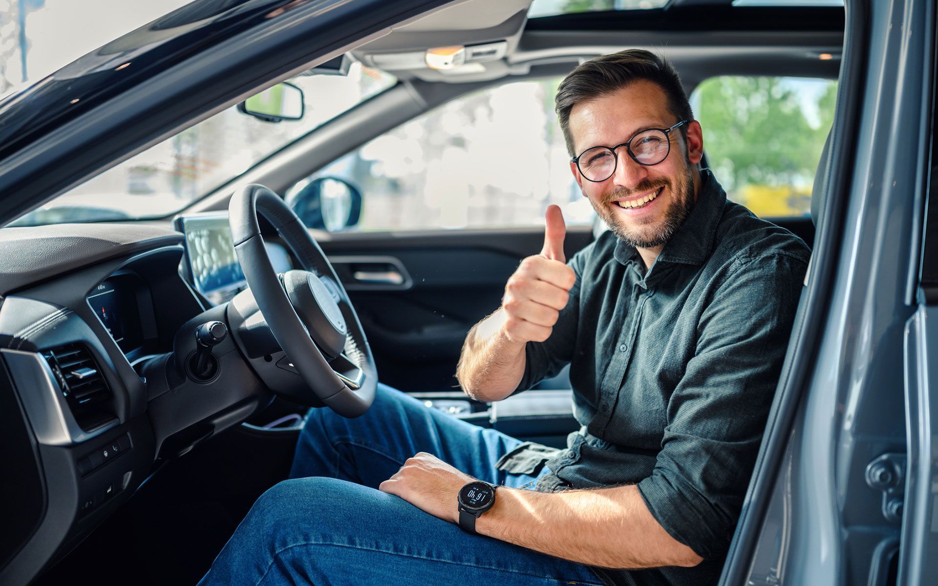 A man is sitting in a car and giving a thumbs up.