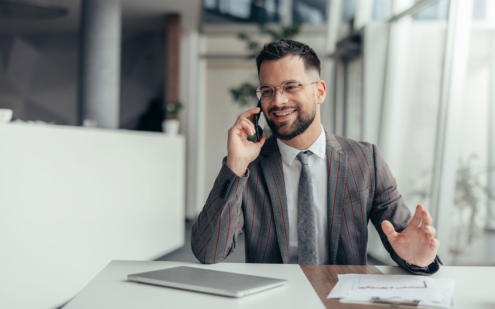 A man is sitting at a desk talking on a cell phone.