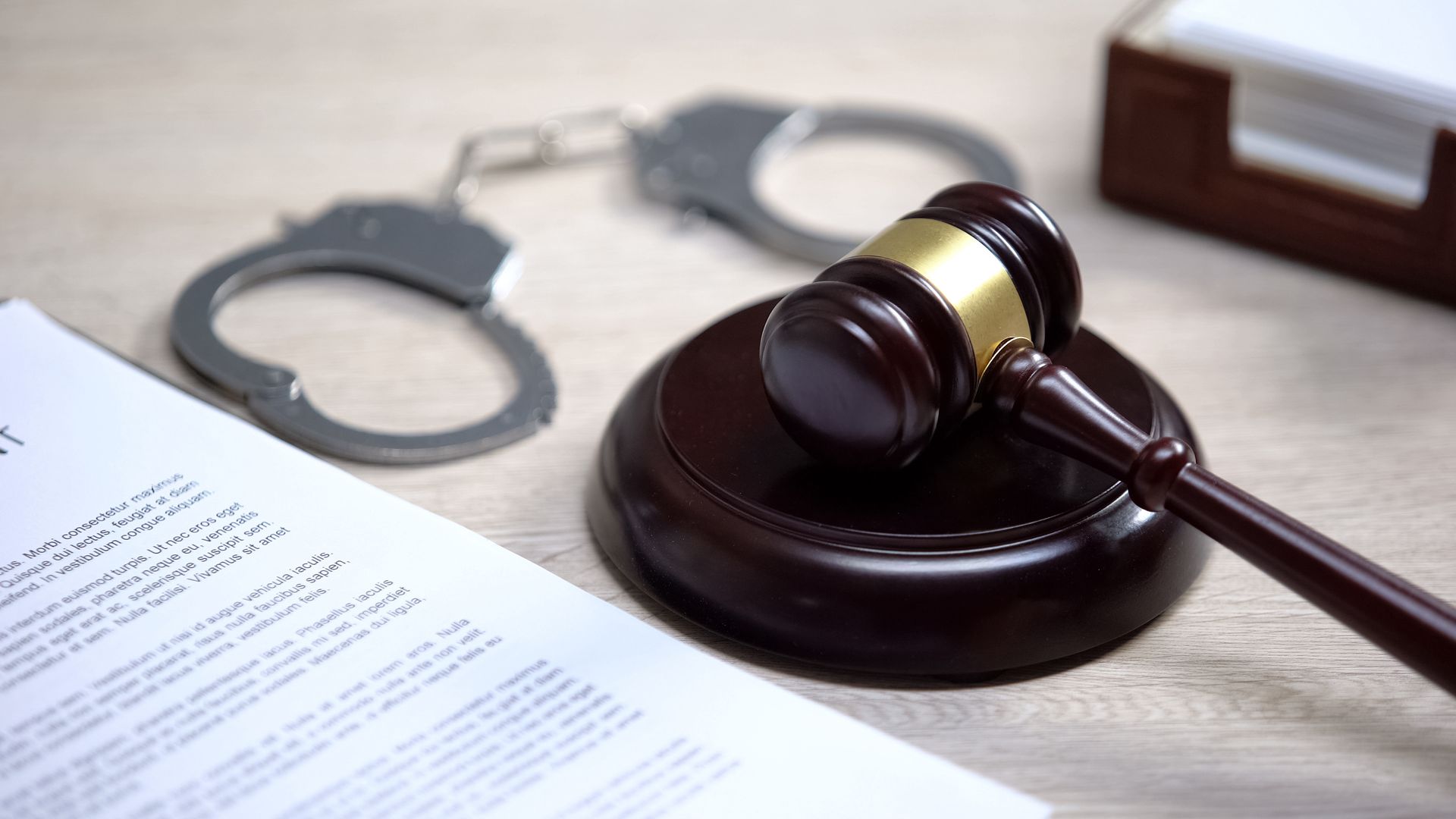 Gavel on a law book beside handcuffs and a document on a desk