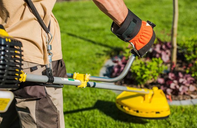 Persona che usa un tagliaerba a filo giallo per tagliare l'erba in un giardino