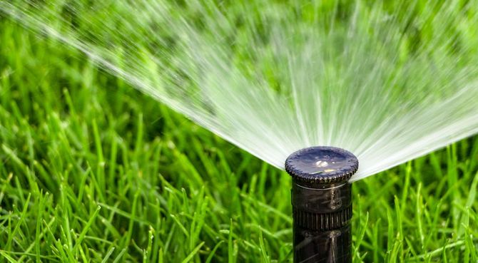 Irrigatore da giardino che spruzza acqua su un prato verde brillante a distanza ravvicinata