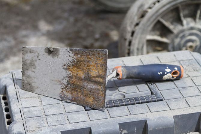 Raschietto e cazzuola di metallo arrugginito su un banco da lavoro ruvido.