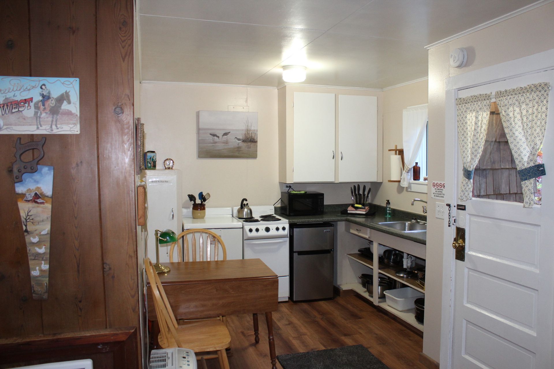 Small kitchen with wood-paneled wall, white cabinets, stove, sink, table, and open doorway.