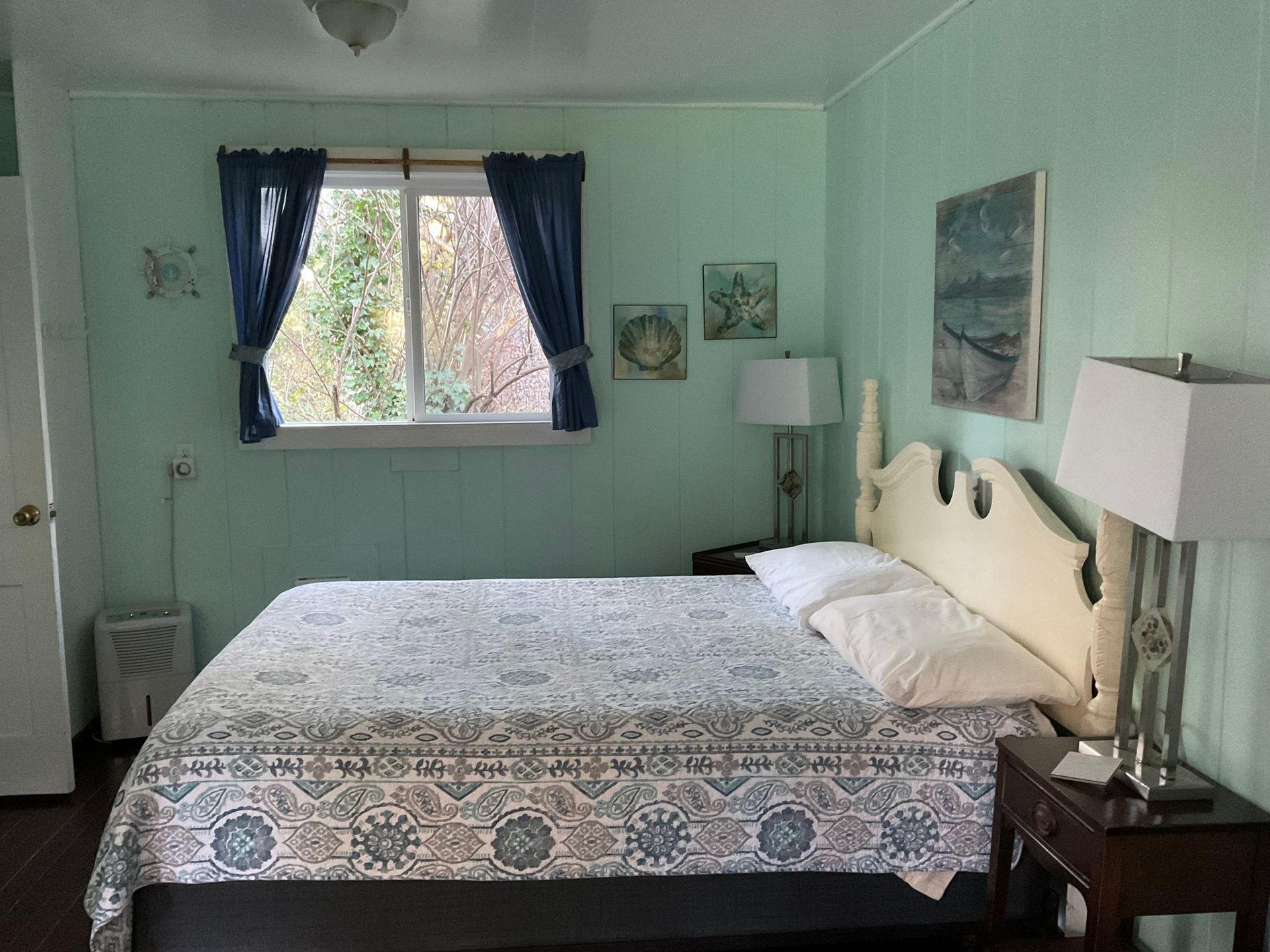 Bedroom with a made bed, mint-green walls, blue curtains, and bedside lamps by a window