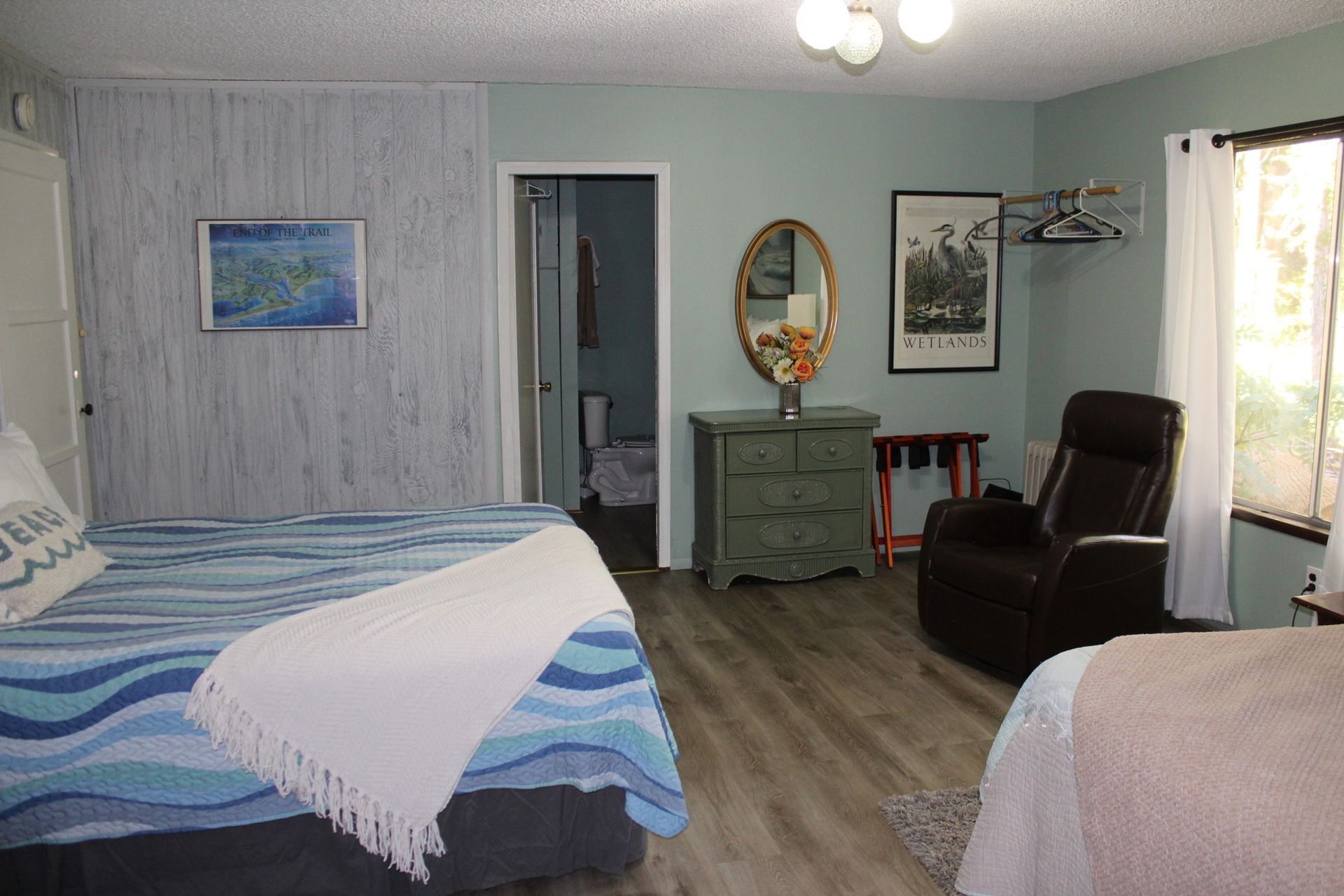 Bedroom with two beds, green dresser, brown chair, and open doorway under soft gray walls.
