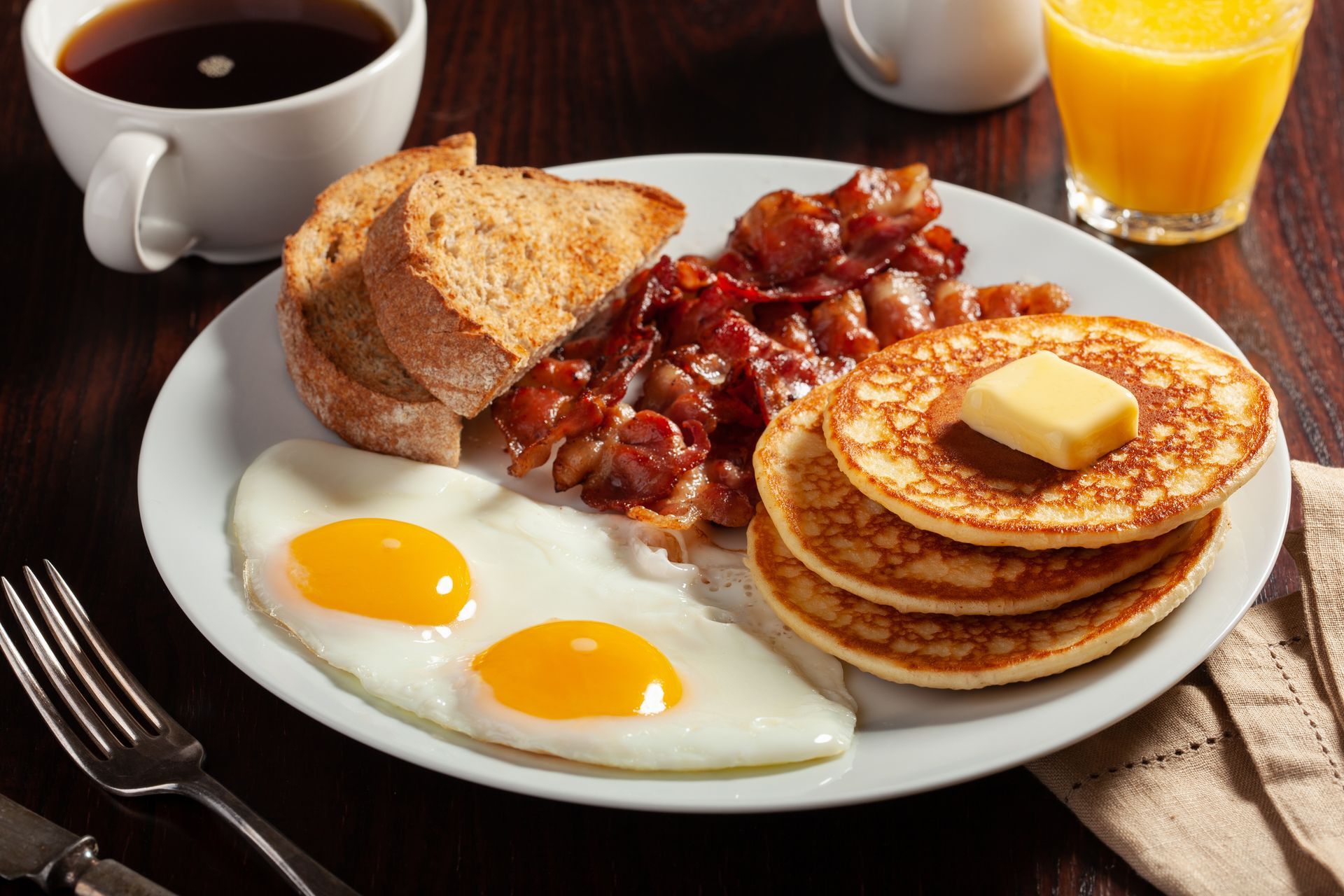 Breakfast plate with pancakes, eggs, bacon, toast, coffee, and orange juice