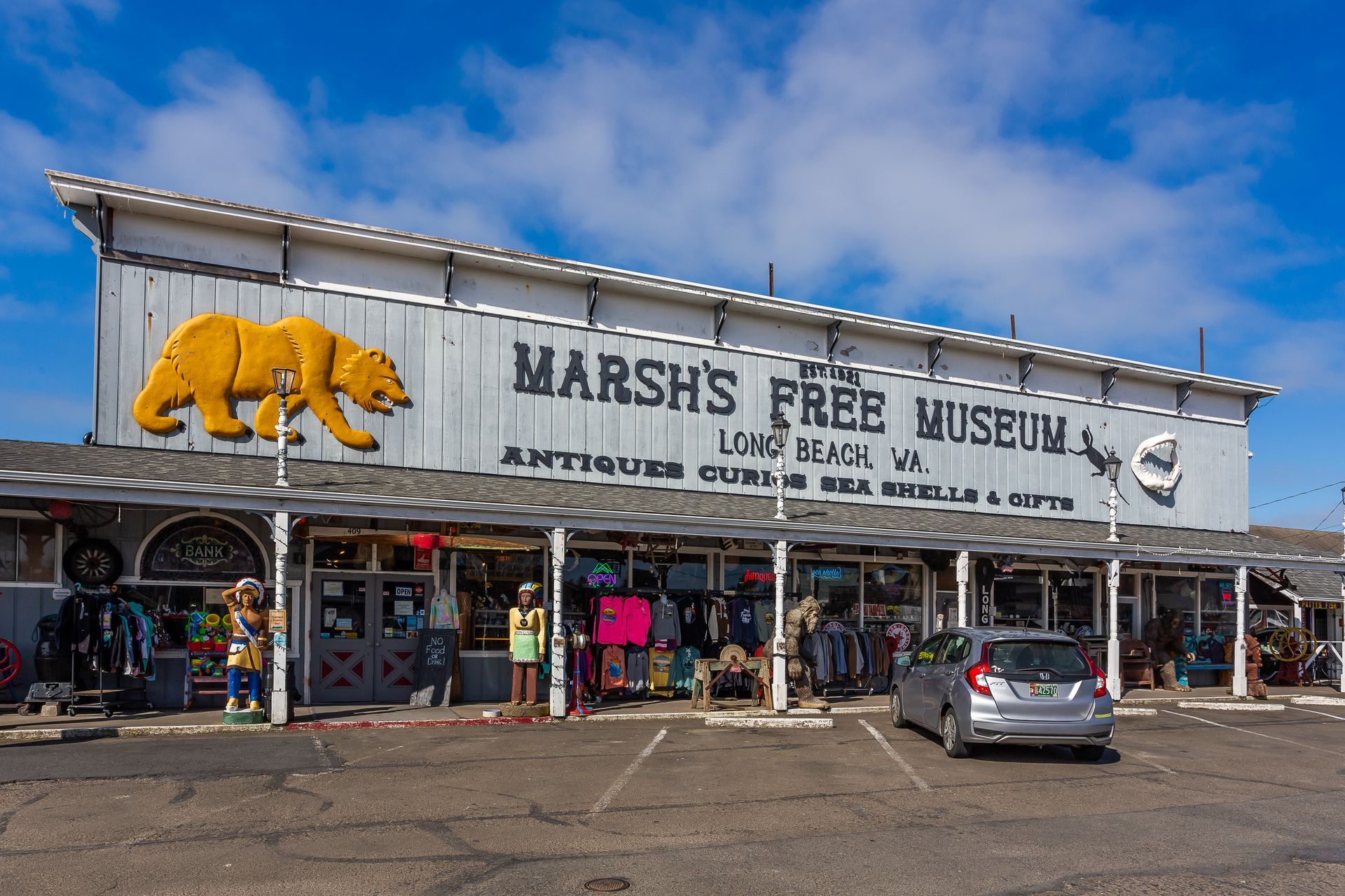 Marsh’s Free Museum storefront with yellow bear sign, souvenir shops, and parked cars under a blue sky