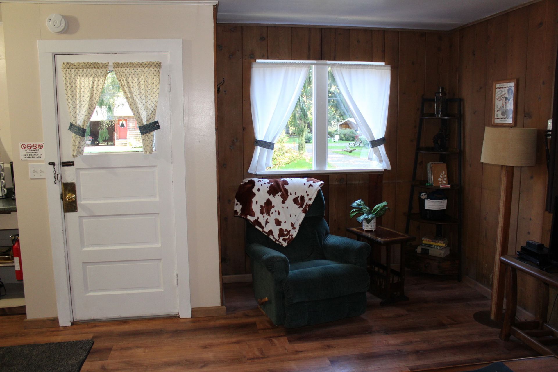 Cozy living room with wood paneling, green chair by a window, and a white door on the left.