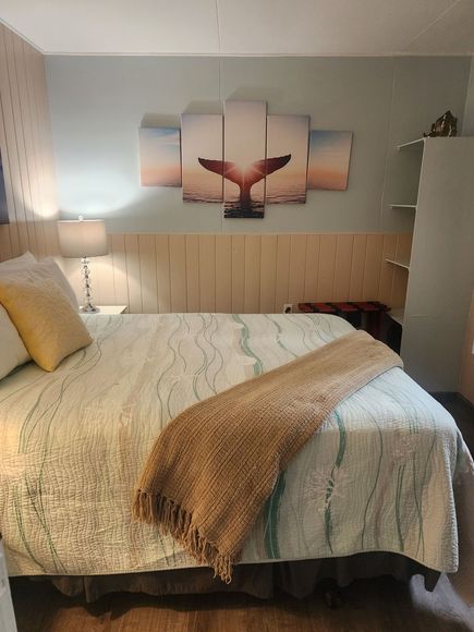 Neatly made bedroom with a bed, lamp, textured pillows, and whale wall art above the headboard
