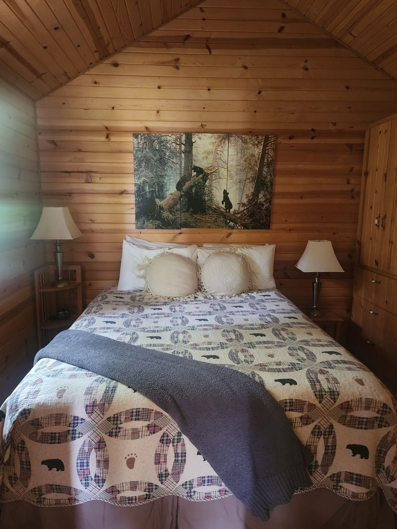 Cozy log cabin bedroom with a bed, lamps, quilt, and forest wall art