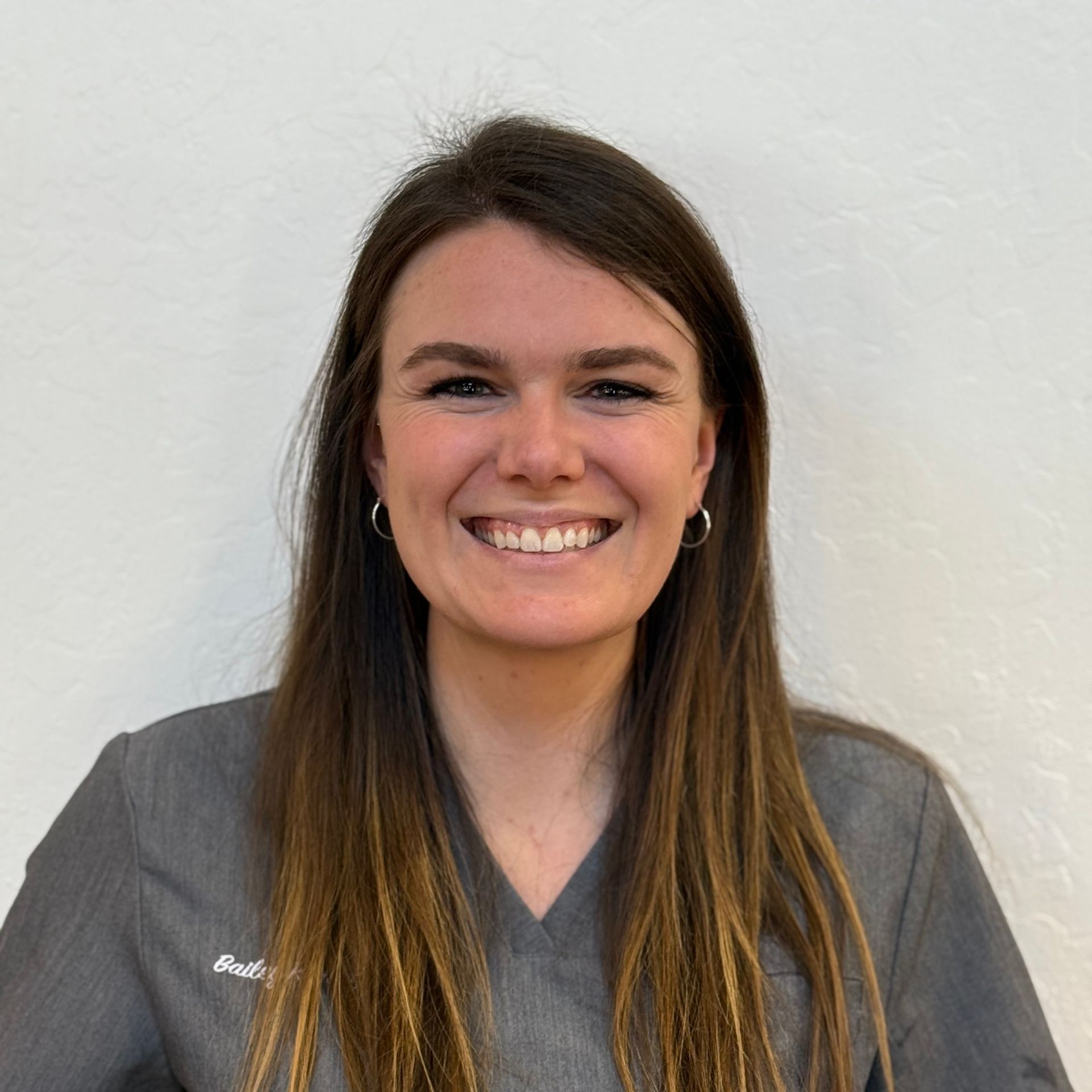 A woman in a gray scrub top is smiling for the camera.