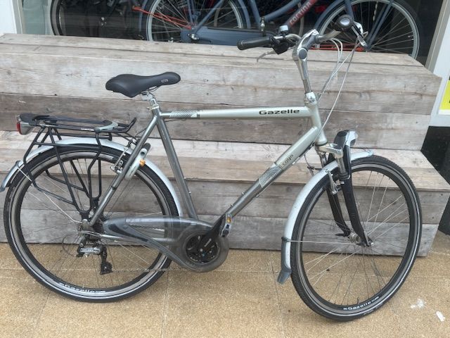 Zilverkleurige fiets met zwarte banden, spatborden en bagagedrager.