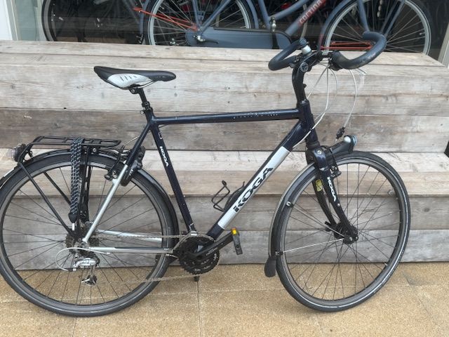 Donkerblauwe Kona toerfiets, zwarte spatborden en bagagedrager, buiten.