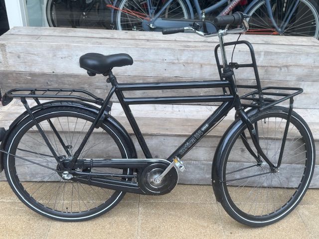 Zwarte fiets in Nederlandse stijl met bagagedragers voor en achter, buiten geparkeerd.