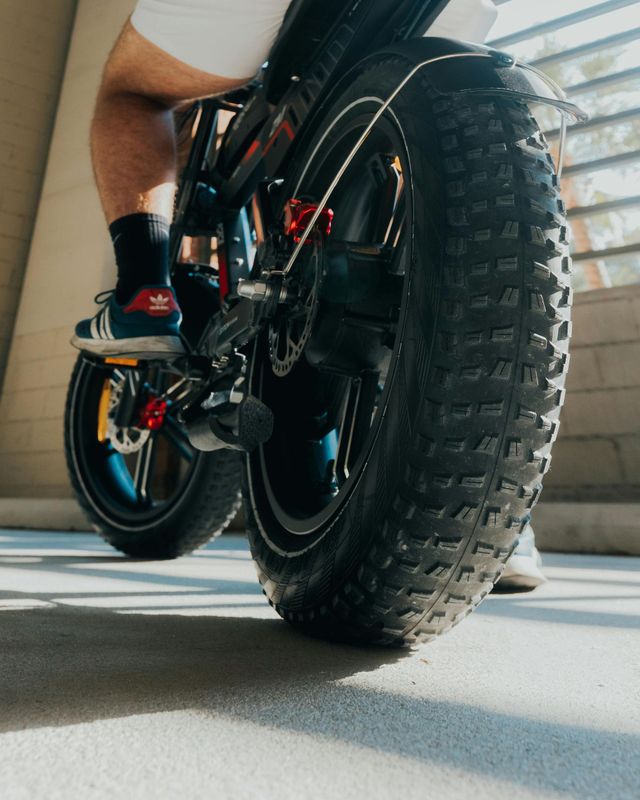 Persoon rijdend op een zwarte elektrische fiets met grote, profielbanden; close-up van het achterwiel.
