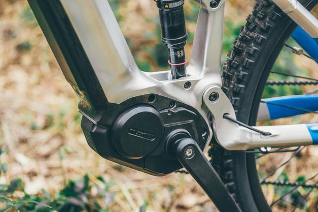 Close-up van de elektromotor en achtervering van een e-bike. Zilverkleurige en zwarte onderdelen, fietswielen op de achtergrond.