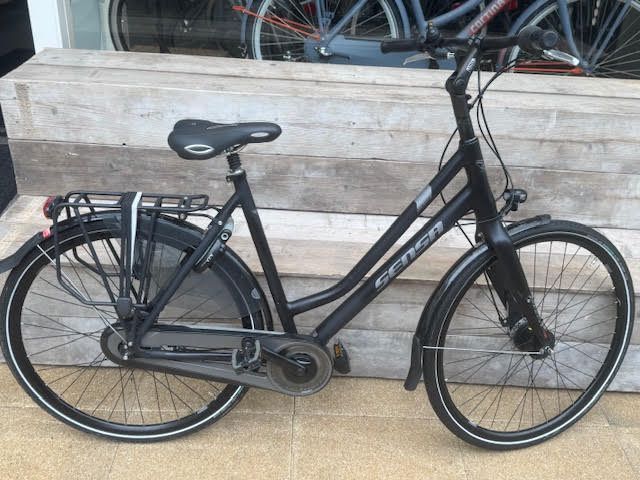 Zwarte stadsfiets met spatborden, bagagedrager en verlichting, buiten geparkeerd.