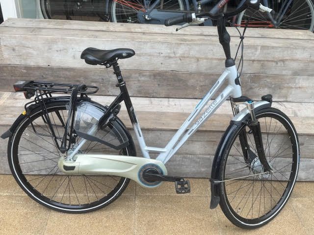 Een zilverkleurige en zwarte stadsfiets met spatborden, bagagedrager en lage instap staat buiten geparkeerd.