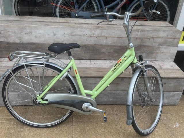 Groene Gazelle-fiets met zilverkleurige spatborden en bagagedrager, buiten geparkeerd.