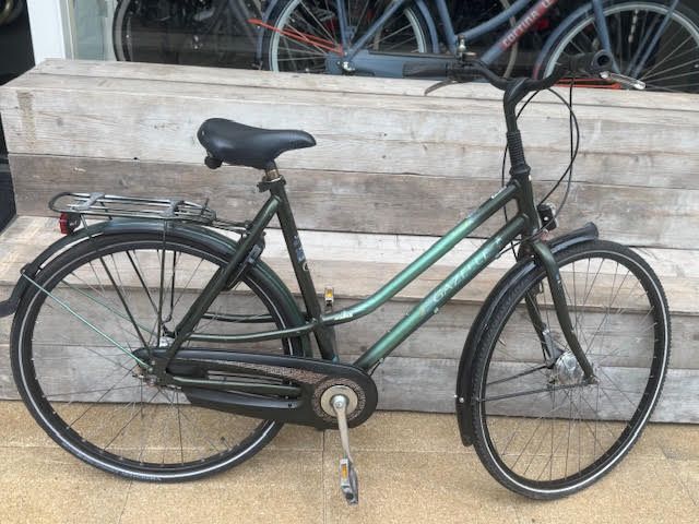 Groene fiets met lage instap, zwarte spatborden en een bagagedrager, buiten geparkeerd.