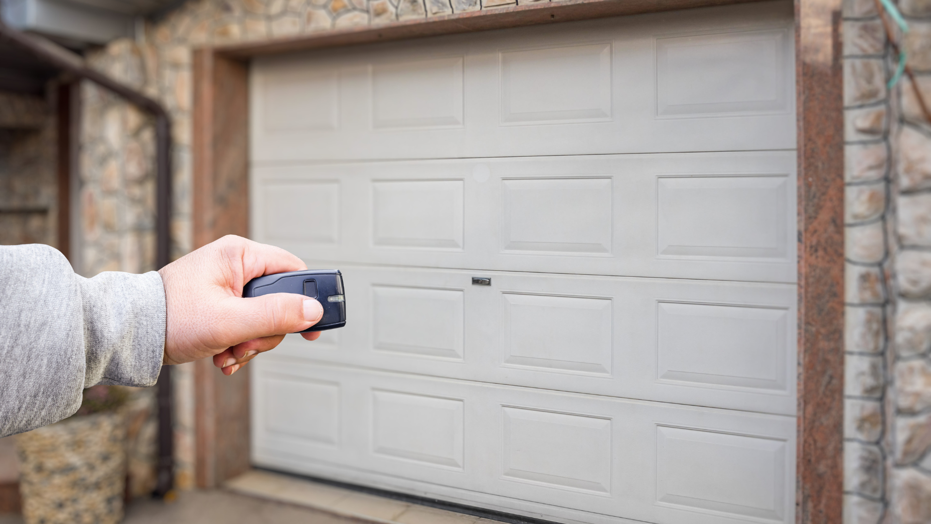 Hand operating a garage door opener remote, opening a beige garage door.