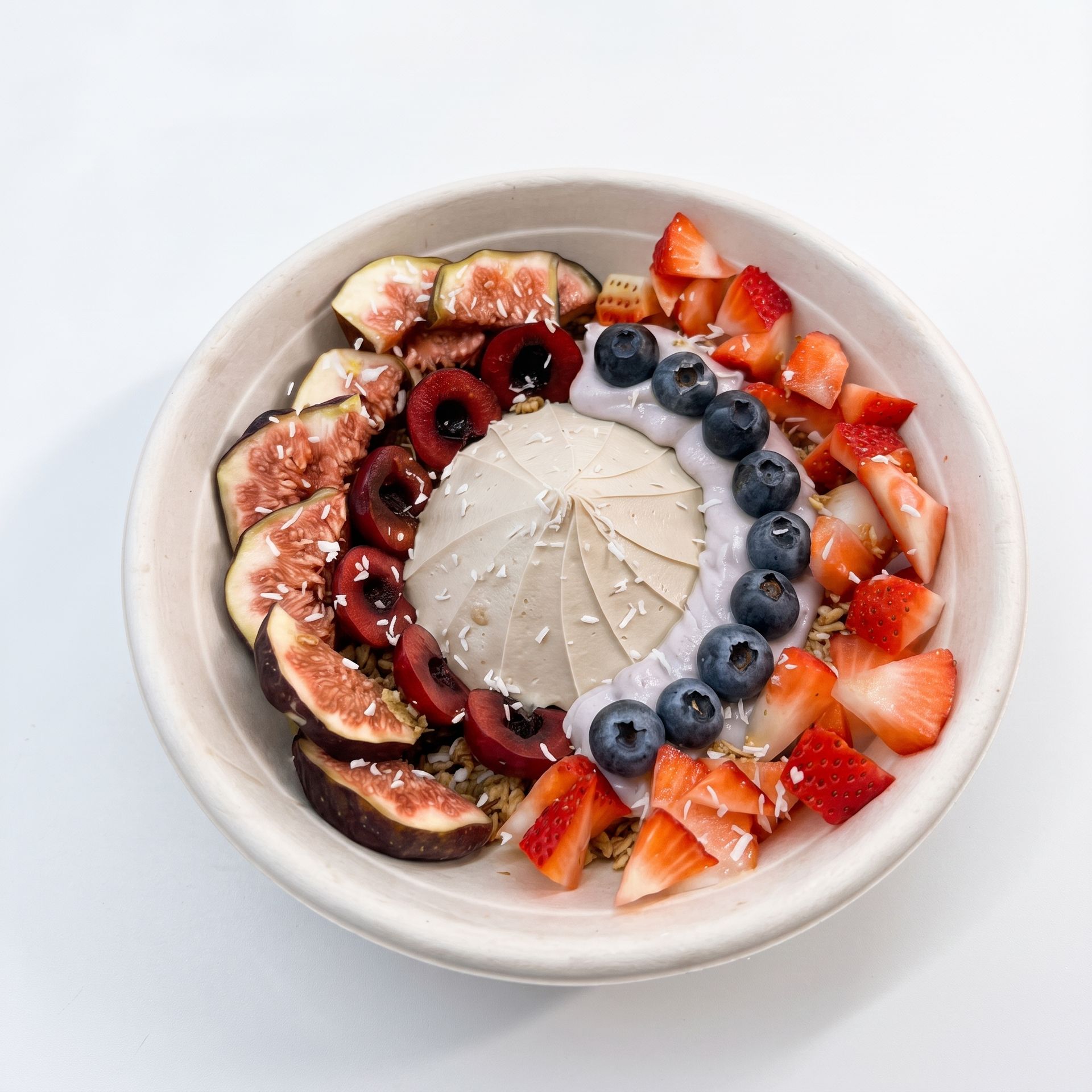 Bowl of dessert topped with figs, blueberries, strawberries, and berry sauce on a white background
