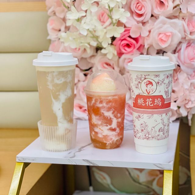 Three takeaway drinks on a small white table with a pink floral backdrop