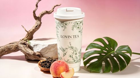 Floral travel cup on white surface with peach, dried flowers, driftwood, and green monstera leaves on pink background