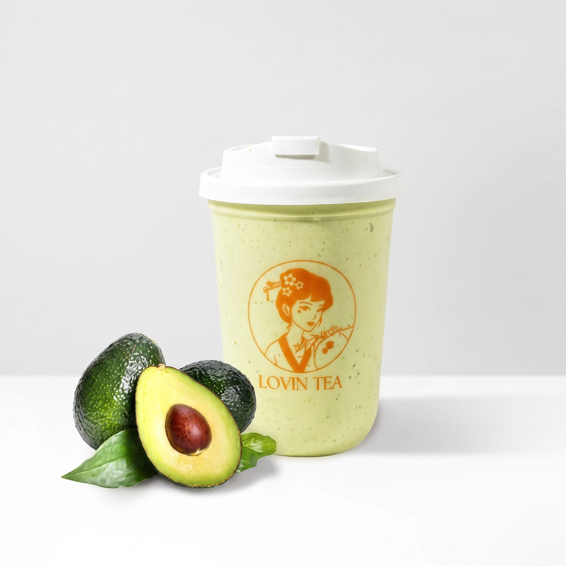 Avocado tea cup with white lid beside whole and halved avocados on a light background