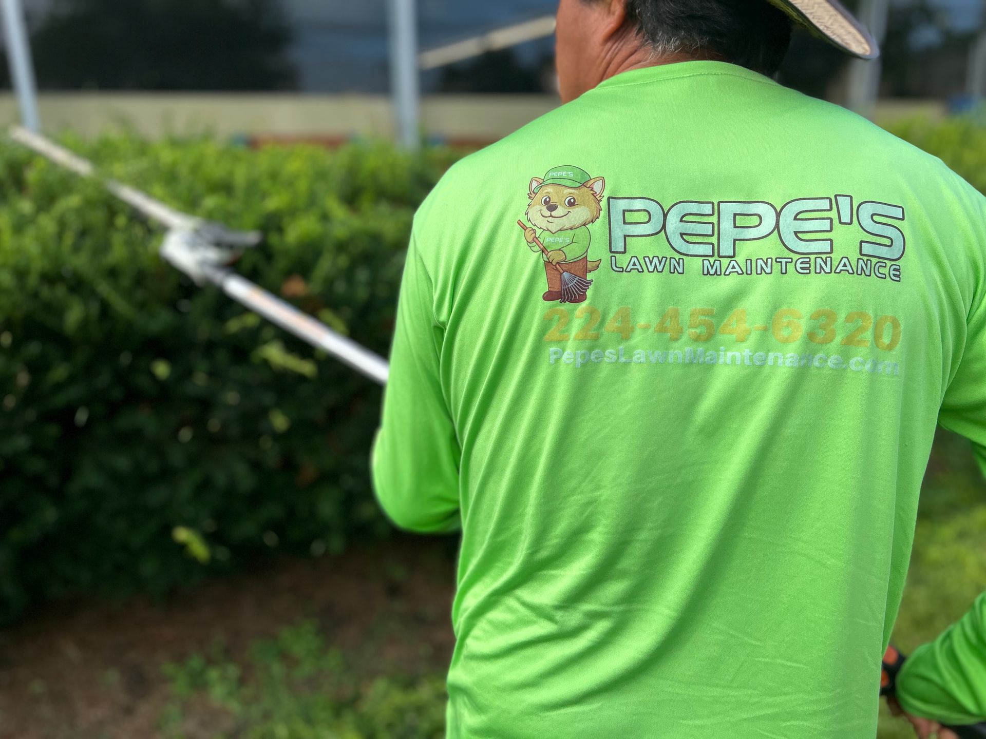 Person in a bright green shirt with a Pepe’s logo, standing outdoors near bushes.