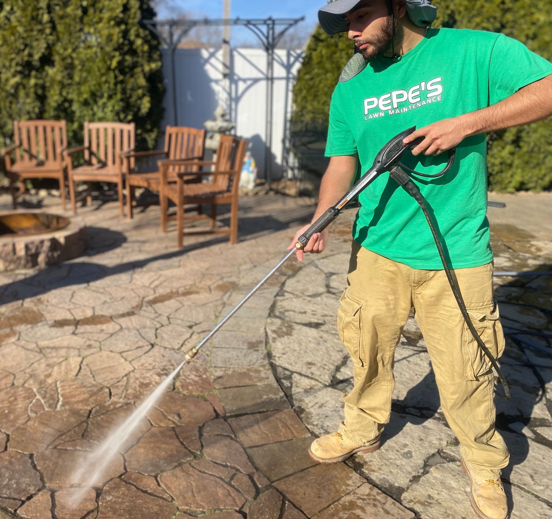 A man is using a high pressure washer to clean a sidewalk.