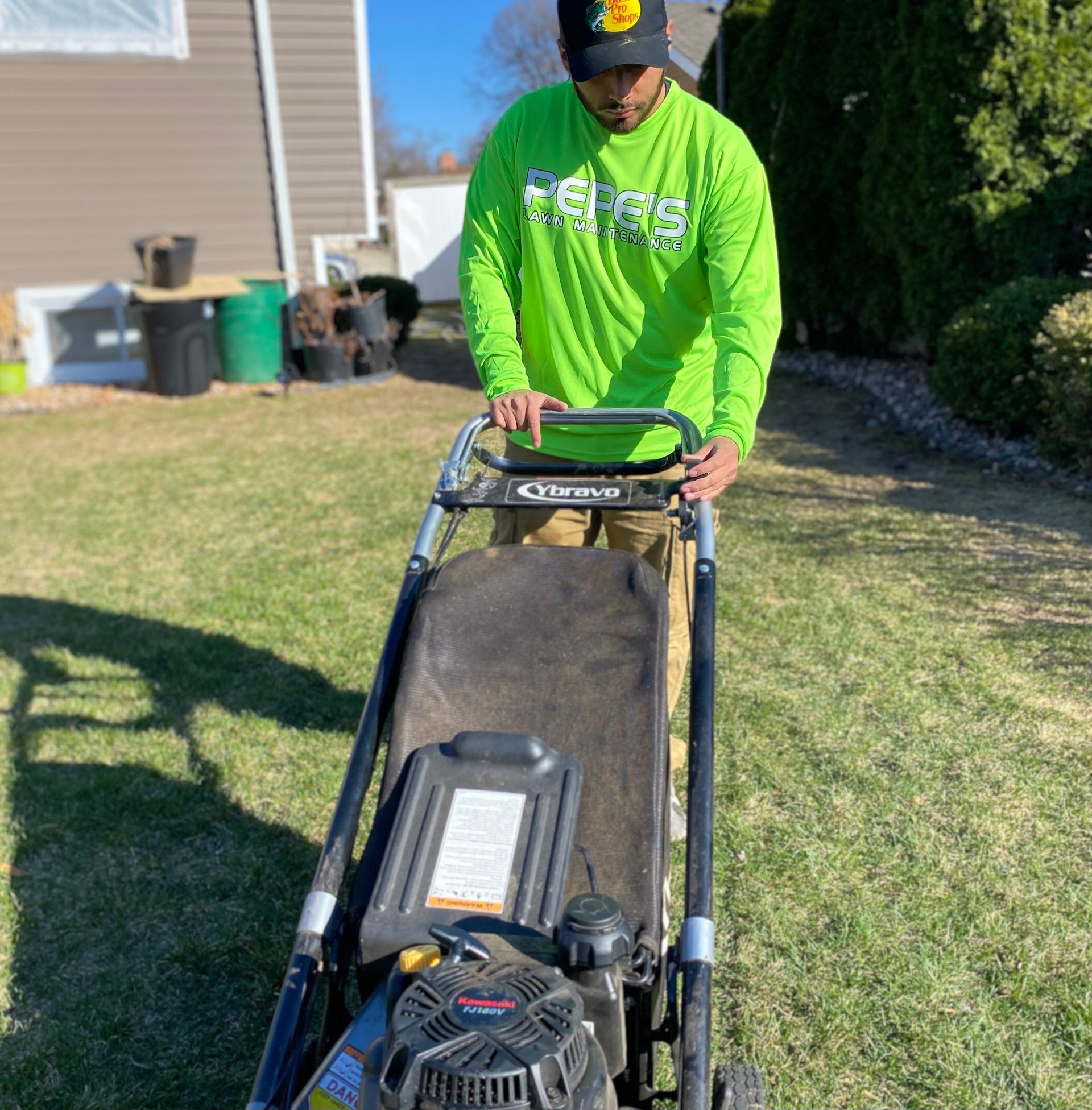 A man in a green shirt is pushing a lawn mower.