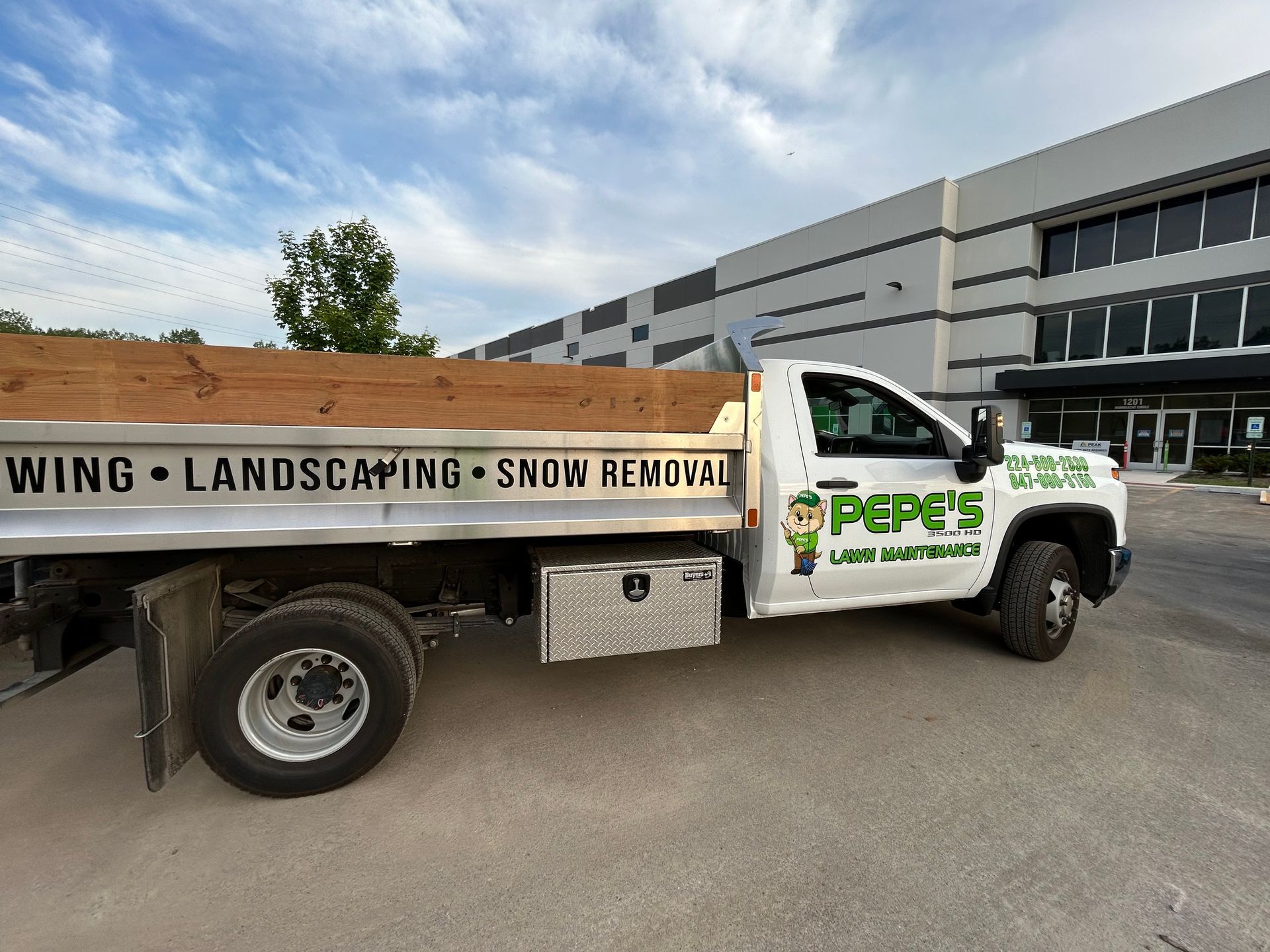 White landscape company truck parked outside an industrial building under a cloudy sky.