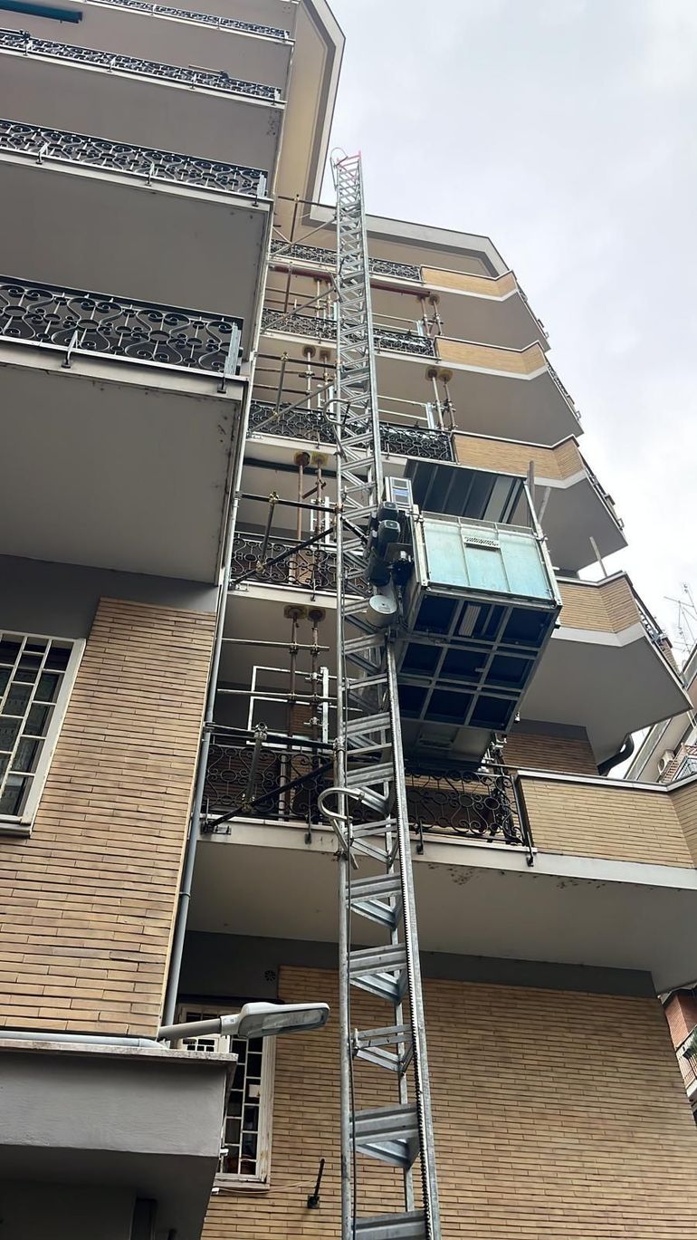 Facciata dell'edificio con montacarichi e ponteggi accanto ai balconi su uno stretto pozzo.