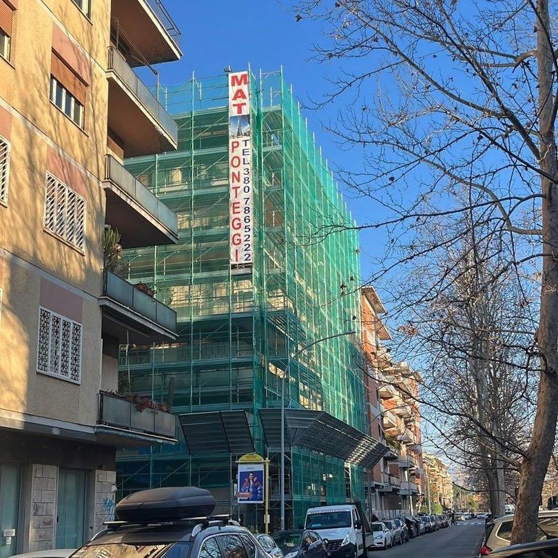 Operai edili con giubbotti arancioni e caschi di sicurezza assemblano impalcature metalliche su un tetto.