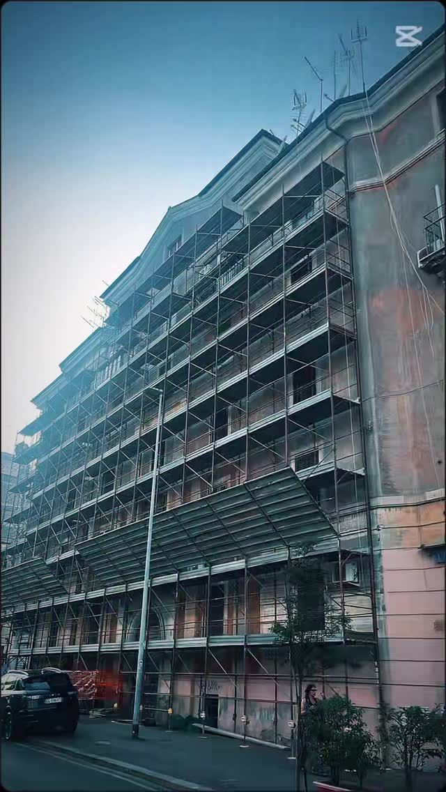 Un antico e alto palazzo residenziale con numerosi balconi, visto dal basso su una strada al crepuscolo.
