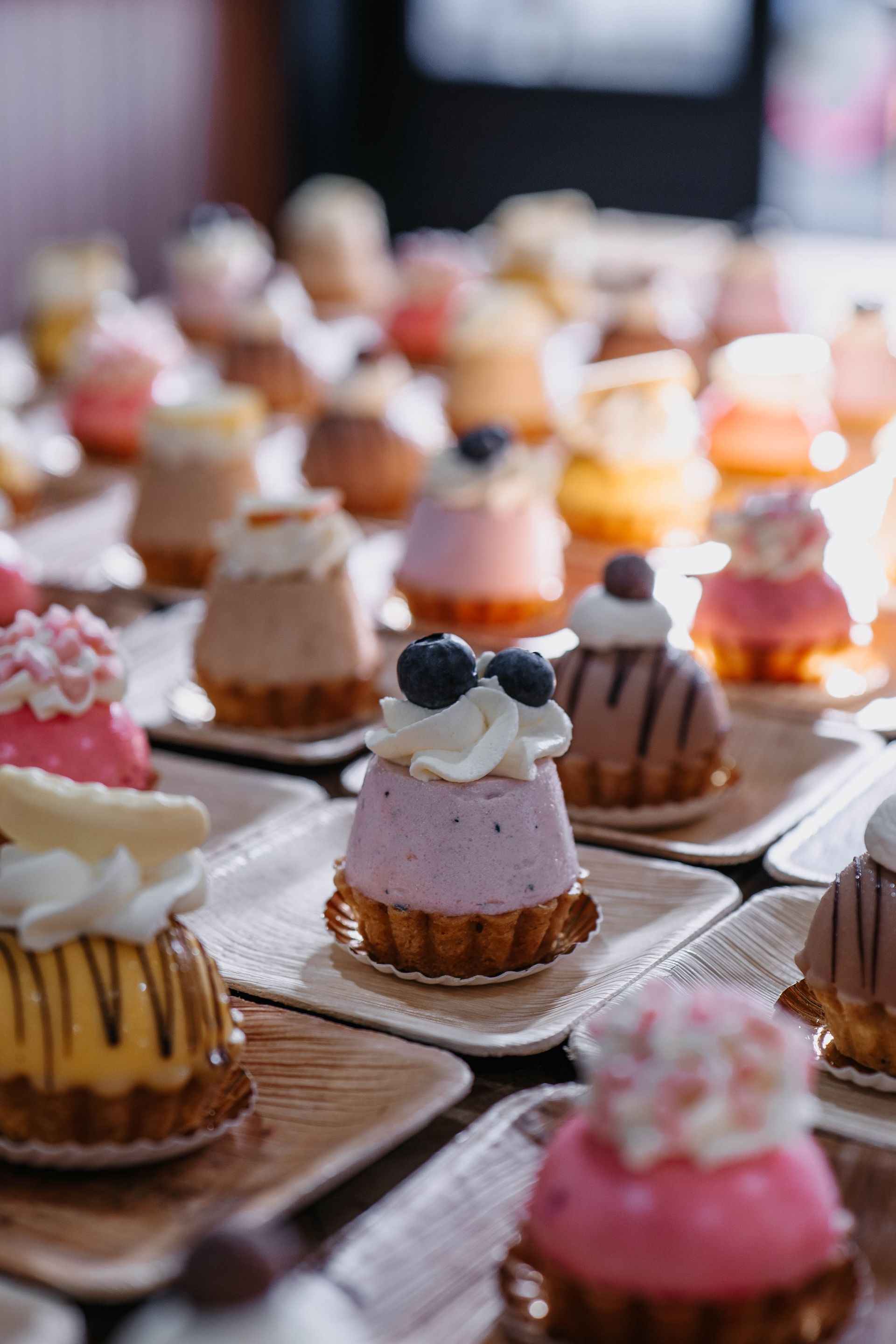 Een opname van bovenaf van vele kleine, kleurrijke, decoratieve gebakjes, gerangschikt op afzonderlijke vierkante bordjes.