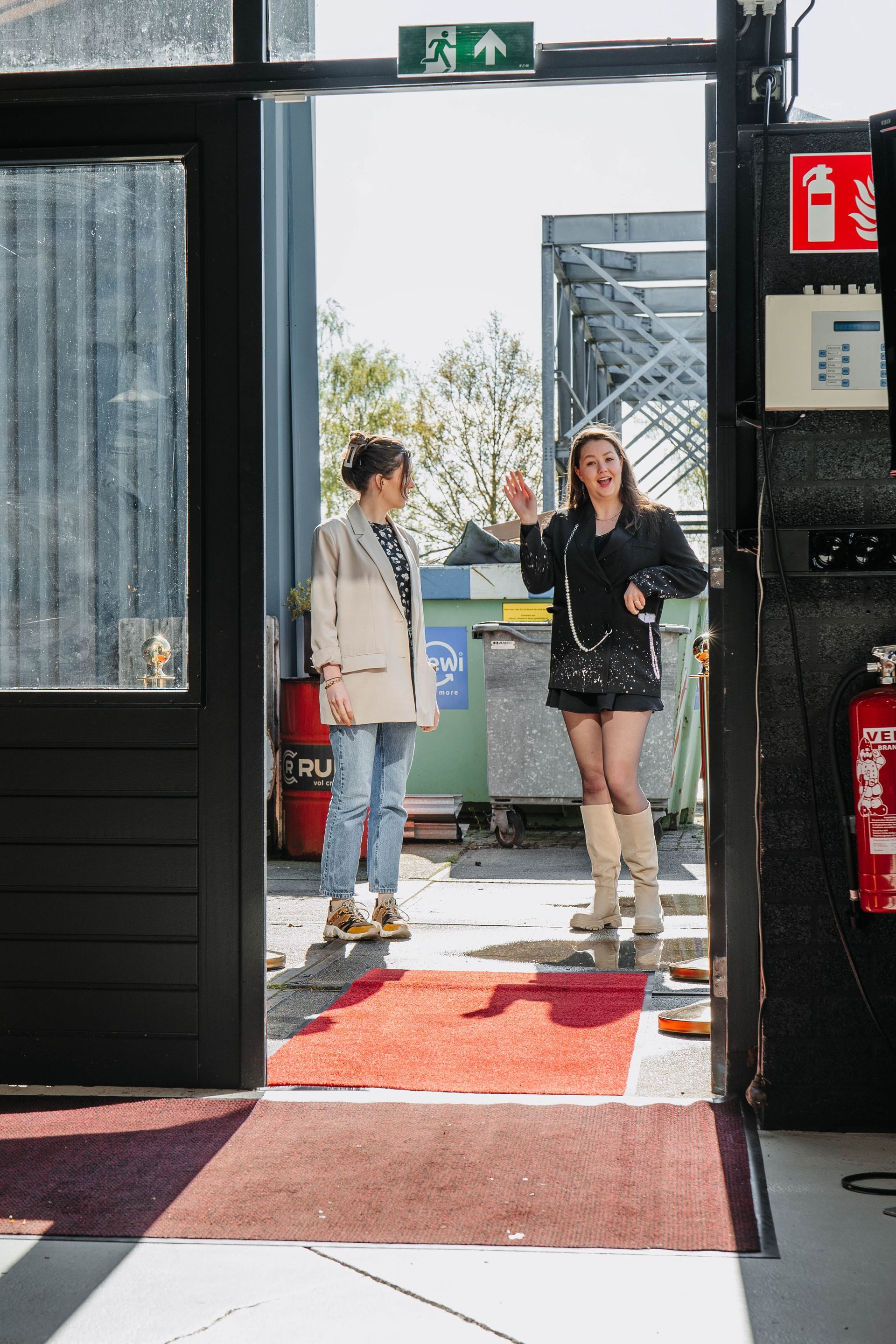 Twee mensen staan ​​tegenover elkaar in een deuropening, de een draagt ​​een licht jasje en een spijkerbroek, de ander een zwart shirt en laarzen.