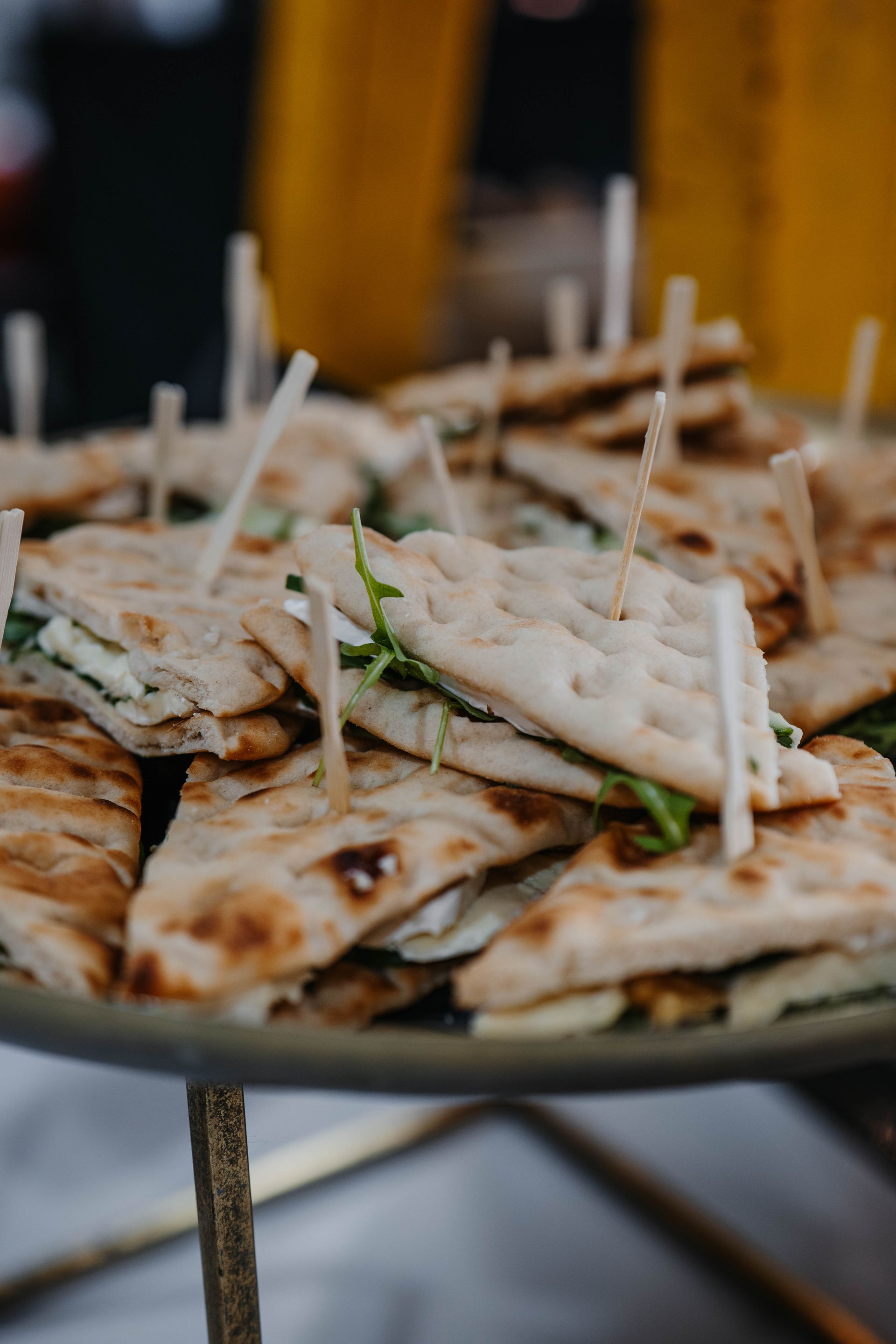 Driehoekige gegrilde platbroodsandwiches met groenten en vulling, gestapeld op een etagère met houten prikkers.