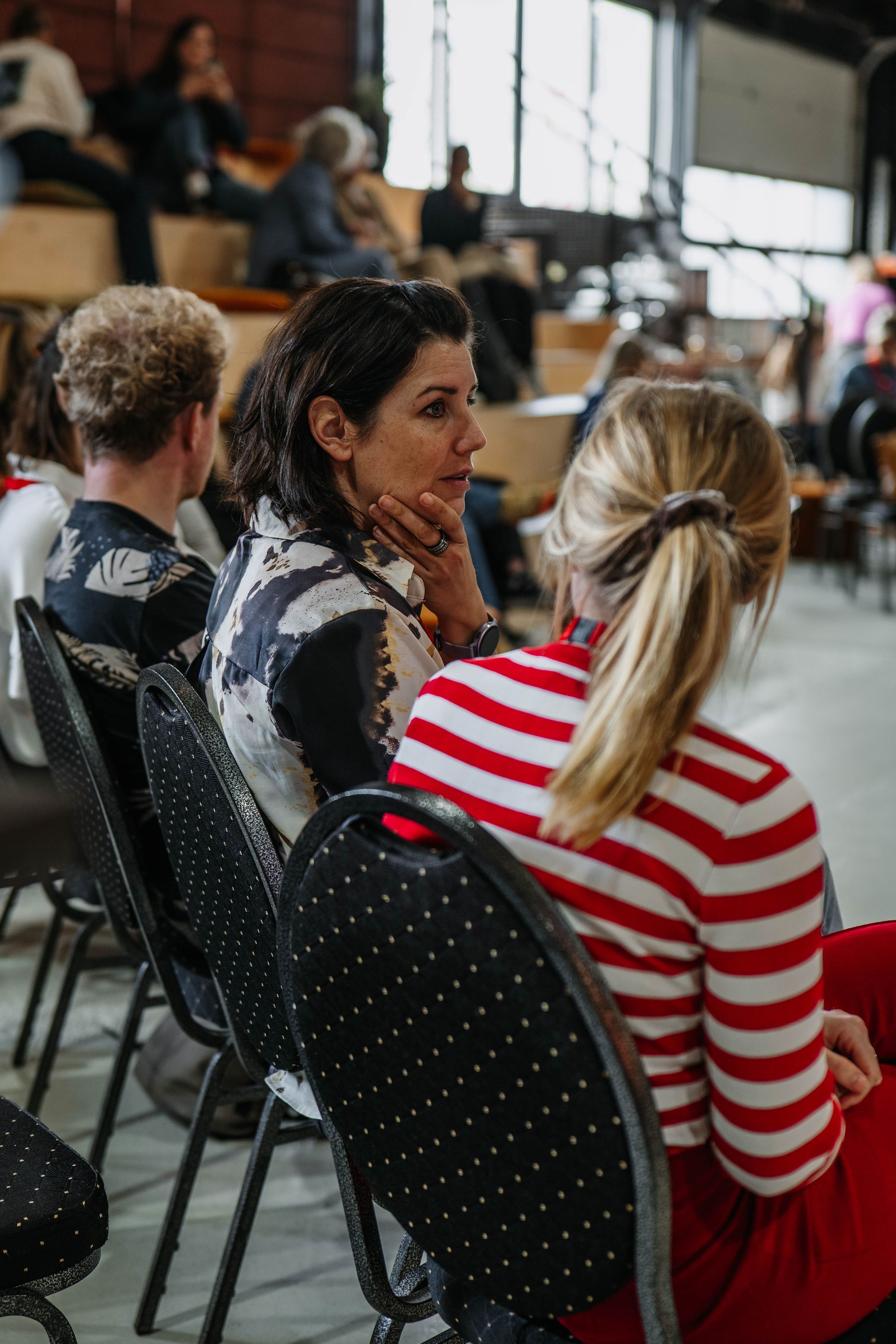 Mensen zitten op stoelen, van achteren gezien, tijdens een workshop of seminar in een ruime, industriële ruimte.