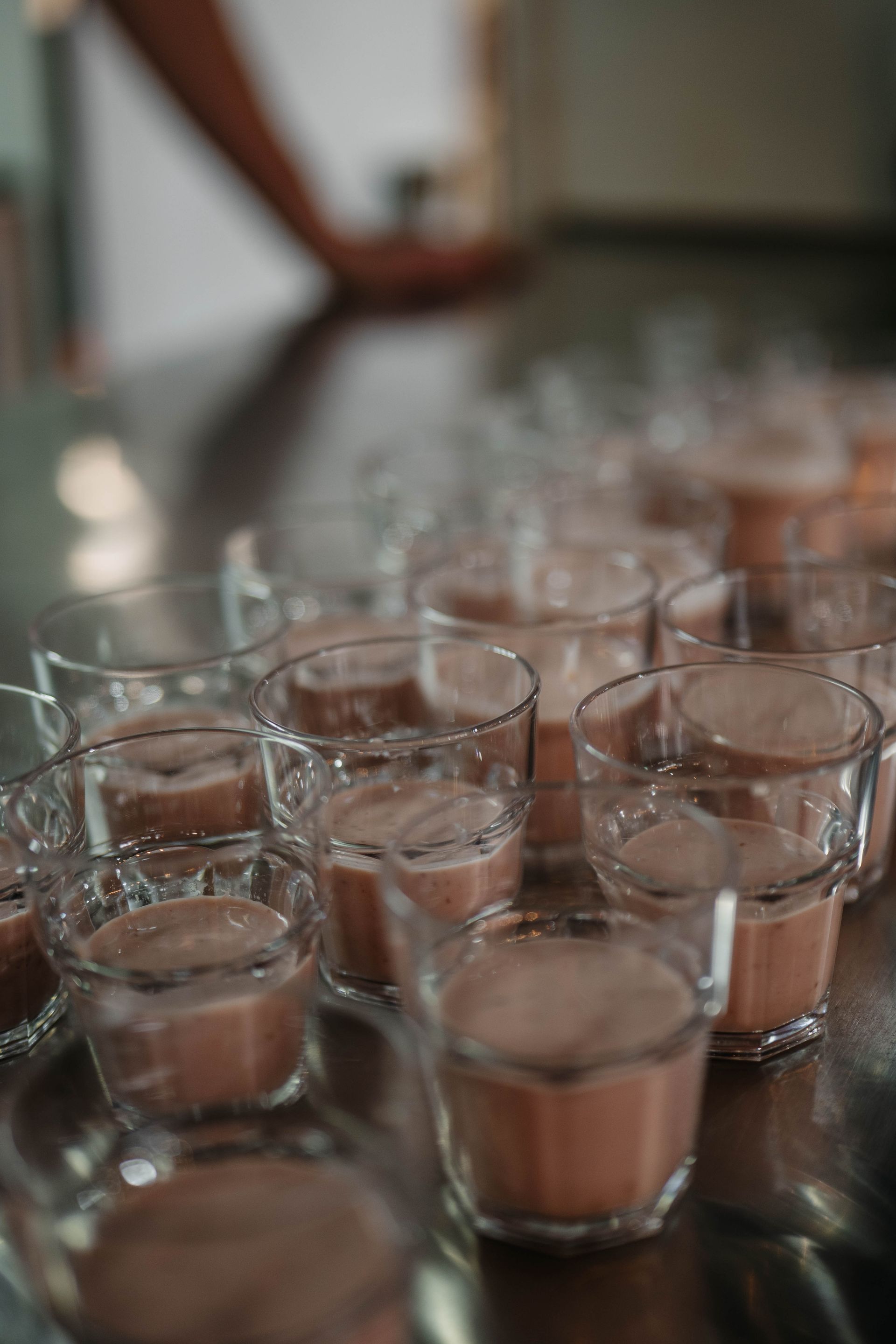 Op een donkere, glanzende tafel staan ​​veel kleine, doorzichtige glaasjes gevuld met een lichtbruine drank.